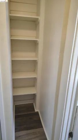 Built-in shelving unit with five white shelves, contrasting with dark wood-finish flooring