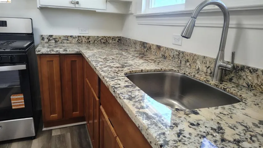 Kitchen featuring a stainless steel sink with a high-arch faucet, granite countertops, wood cabinetry, and a range oven