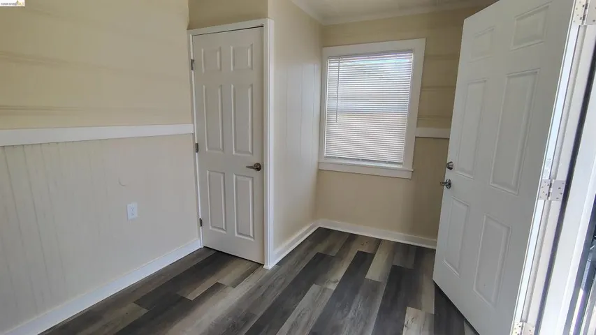 Interior room featuring wood-finish flooring, two white paneled doors, and a window with horizontal blinds