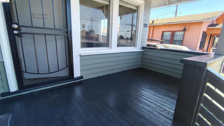Covered porch featuring dark-stained wood-finish flooring, light green horizontal siding, and a white-trimmed window