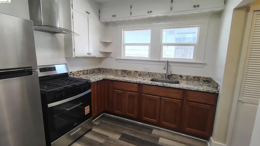 Kitchen with stainless steel appliances, wood-finish flooring, granite-style countertops, and white upper cabinetry