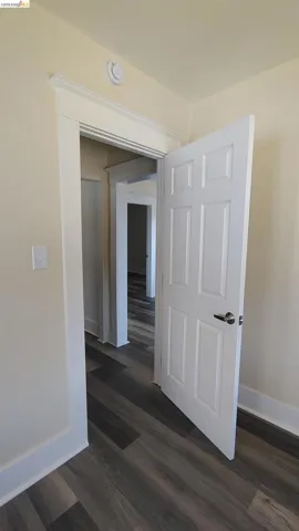 Hallway featuring wood-finish flooring, white trim, and a paneled interior door with satin nickel hardware