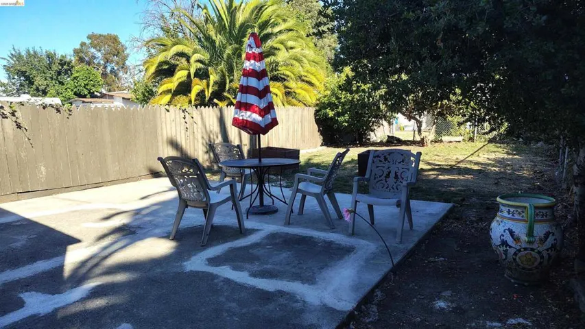 Spacious patio with a concrete surface, bordered by a wooden fence and lush foliage