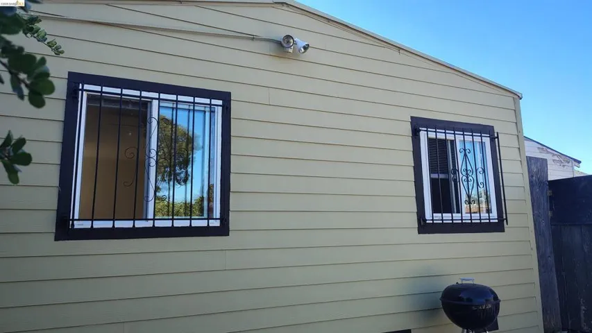 Exterior wall with horizontal siding, featuring two windows with dark security bars