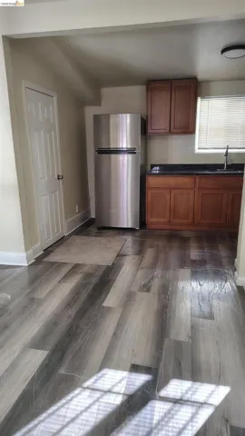 Galley-style kitchen featuring wood-finish flooring, two-tone cabinetry, dark countertops, and a stainless steel refrigerator