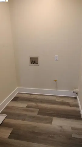 Utility space featuring wood-finish flooring, light-toned wall paint, white baseboards, and a washer hookup