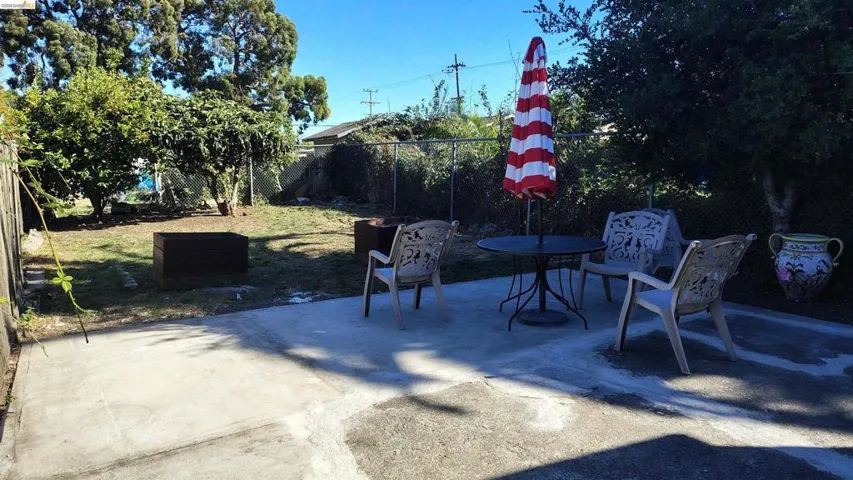 Spacious backyard featuring a concrete patio, mature trees, and wooden raised garden beds