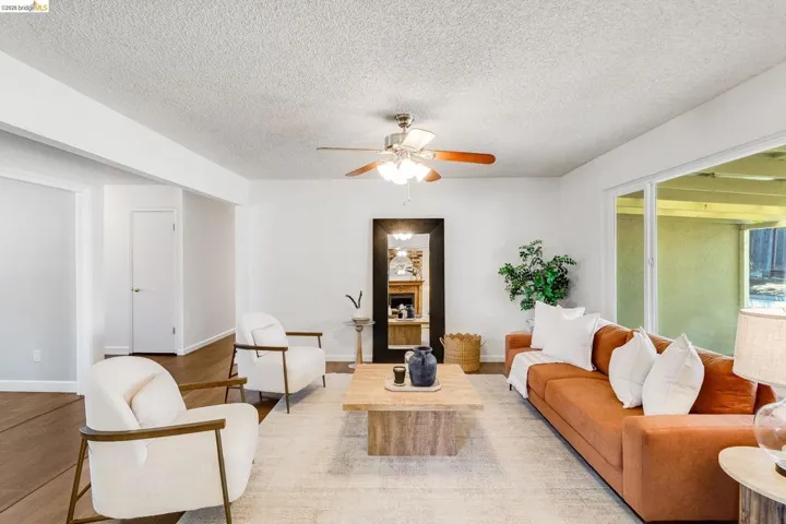 Open concept living space featuring a ceiling fan with integrated lighting, wood-finish flooring, white walls, and sliding glass doors