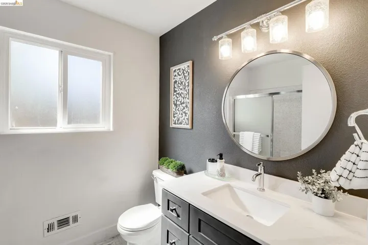 Bathroom featuring a dark accent wall, white vanity with integrated sink, chrome faucet, and a round frameless mirror