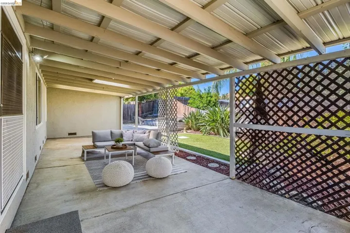 Covered patio featuring a solid roof structure with exposed beams, concrete flooring, and a decorative lattice screen