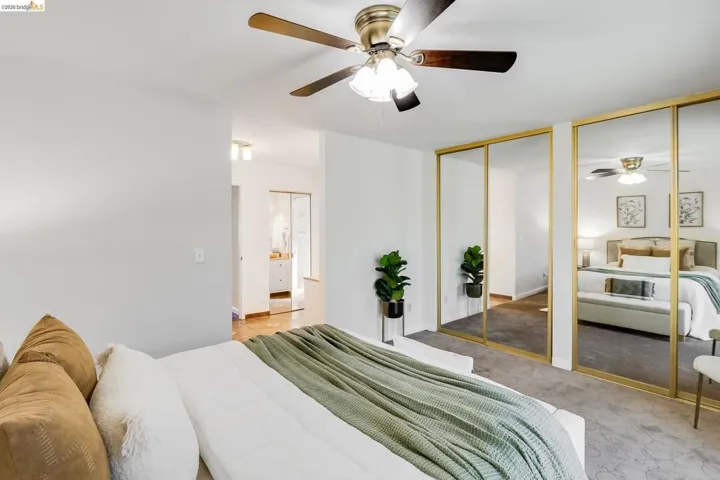 Recessed mirror closet doors with gold-tone framing, a ceiling fan with light fixture, and light gray carpeted flooring