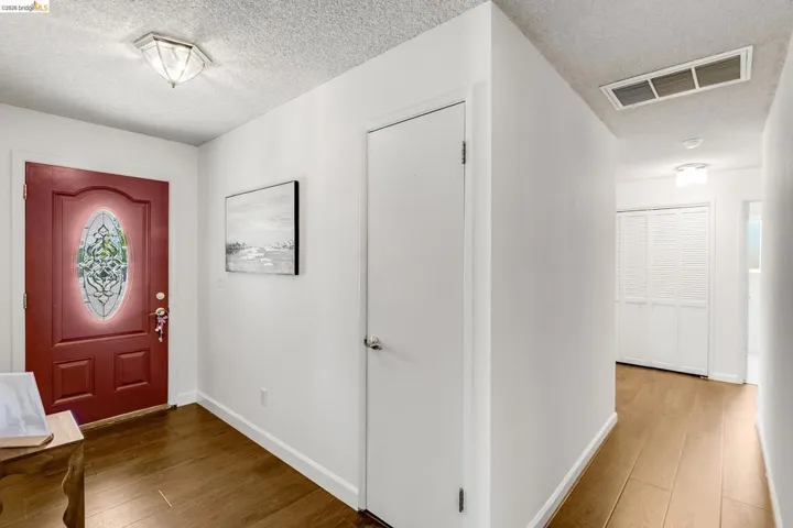 Entryway featuring a red front door with an oval decorative glass insert, wood-finish flooring, and white painted walls
