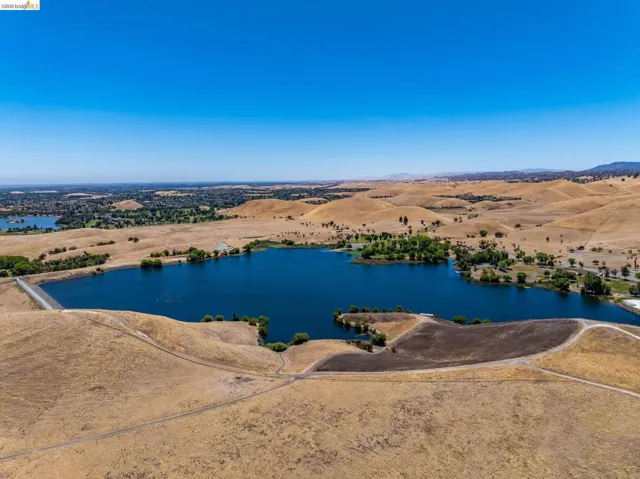 Expansive aerial perspective showcasing a large body of water surrounded by rolling, golden hills