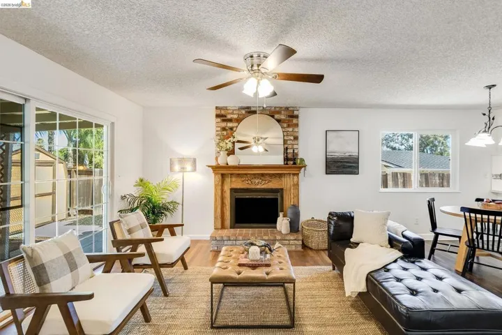 Living area featuring a brick-surround fireplace with a carved wood mantel, wood-finish flooring, and a ceiling fan