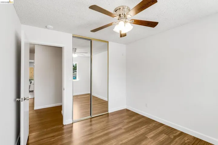 Room featuring wood-finish flooring, a ceiling fan with light fixture, and mirrored closet doors