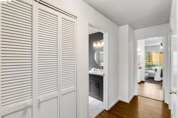 Hallway featuring wood-finish flooring, white louvered bifold closet doors, and smooth white walls