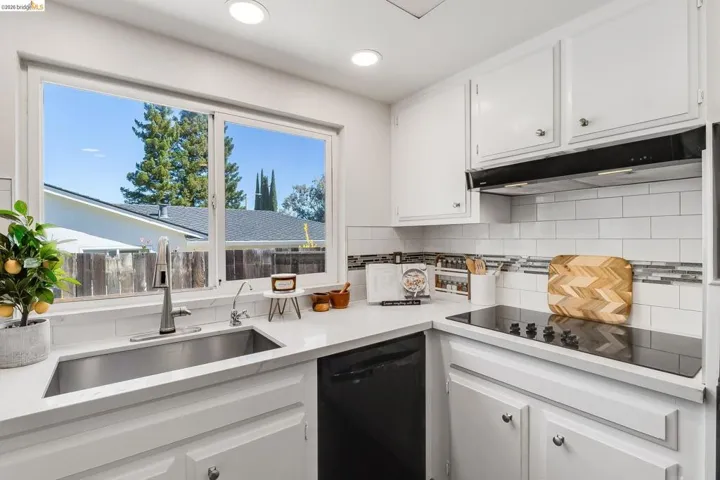 Kitchen featuring a stainless steel undermount sink, quartz countertops, white cabinetry, a subway tile backsplash with decorative accents, and a built-in cooktop