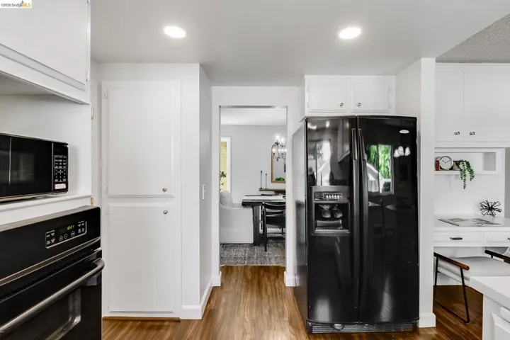 Kitchen featuring wood-finish flooring, recessed lighting, white cabinetry, a built-in oven, and a black side-by-side refrigerator