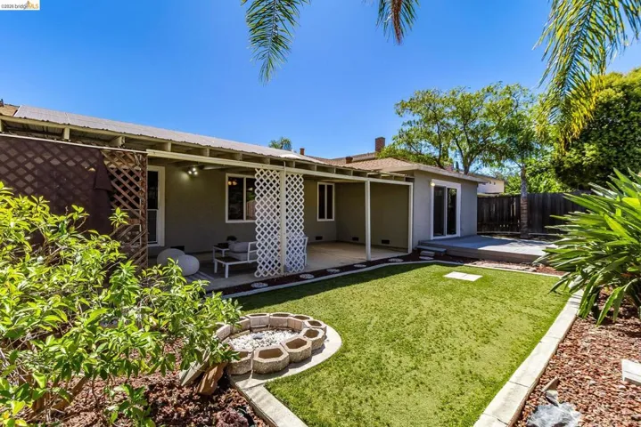 Expansive backyard featuring artificial turf, a concrete fire pit, and a covered patio area with lattice accents