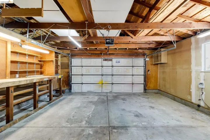 Spacious garage featuring exposed wood beam ceilings, concrete flooring, a paneled garage door, built-in shelving, and a workbench