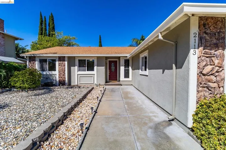 Single-story residence featuring a red entry door, stucco exterior, and natural stone veneer accents