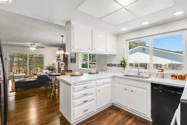 Kitchen featuring white cabinetry, light countertops, integrated sink with gooseneck faucet, and a black dishwasher