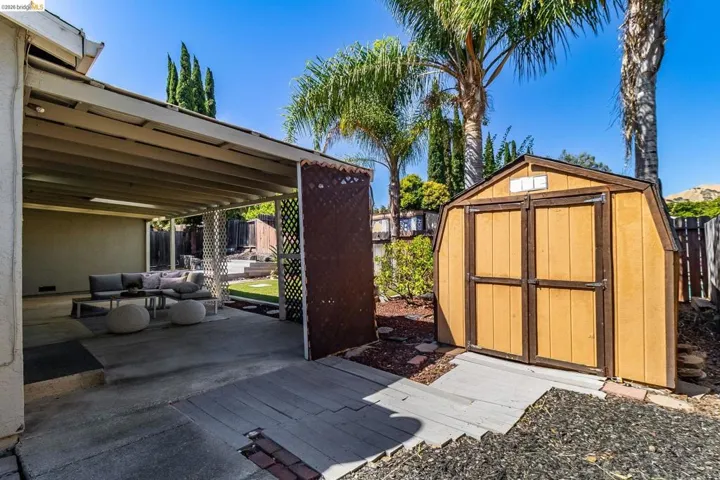 Covered patio area with a concrete slab, lattice privacy screen, and a detached storage shed