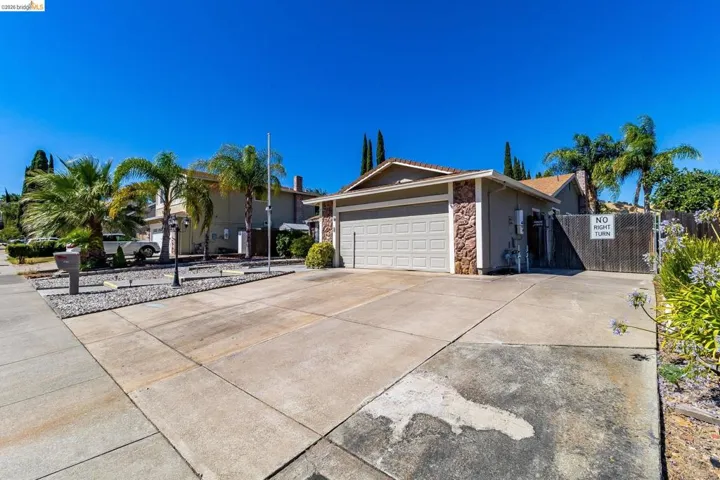 Front exterior featuring a two-car garage, stone facade accents, and mature palm trees