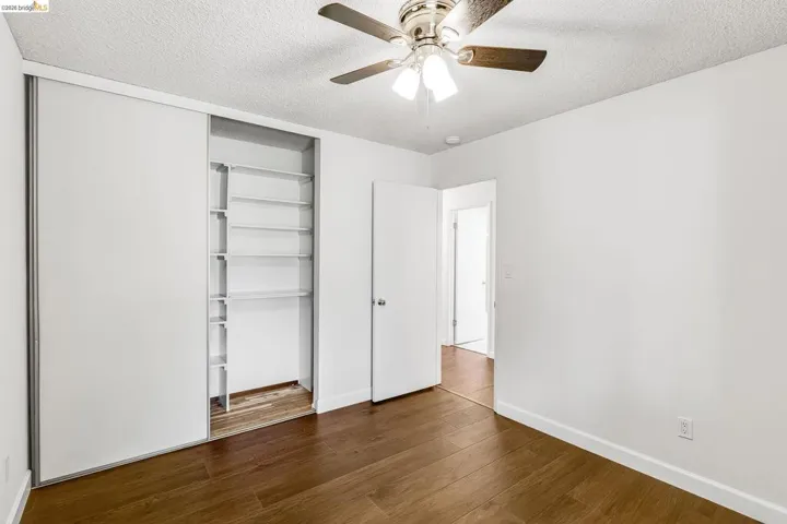 Spacious room featuring wood-finish flooring, white walls, and a ceiling fan with integrated lighting