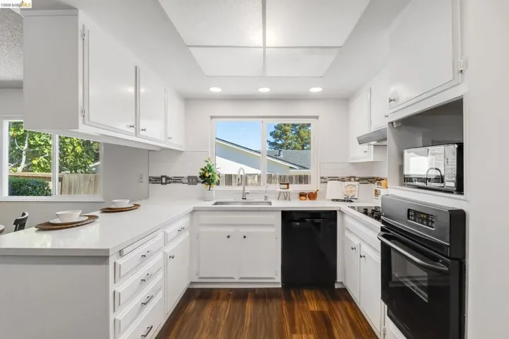 Bright kitchen featuring white cabinetry, light countertops, wood-finish flooring, a stainless steel sink, and black appliances