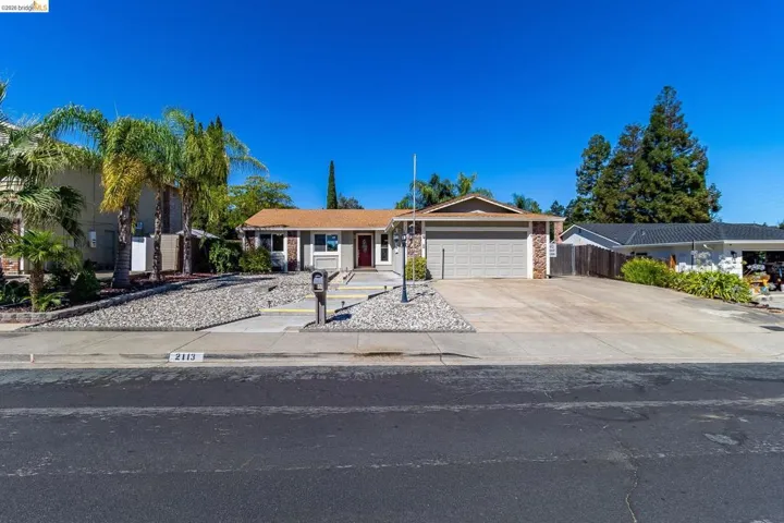 Ranch-style exterior with a two-car garage, concrete driveway, and a red front door