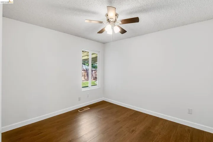 Bright interior space featuring a window with a backyard outlook, wood-finish flooring, white baseboards, and a ceiling fan with integrated lighting