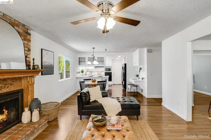 Living area featuring wood-finish flooring, a brick fireplace with a carved wood mantel, and an overhead ceiling fan