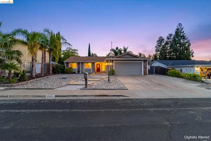 Single-story residence featuring a two-car garage with a brick accent wall, a concrete driveway, and a red front door