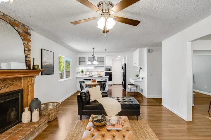 Open-concept living area featuring wood-finish flooring, a brick fireplace with a carved wood mantel, and a ceiling fan