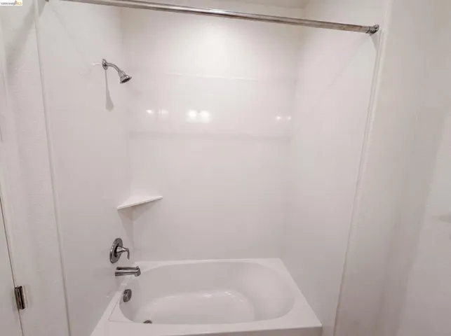 White bathtub with integrated shower, chrome fixtures, and a corner shelf