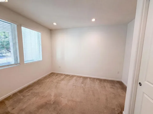 Carpeted room featuring two windows with blinds, recessed lighting, and a white paneled door