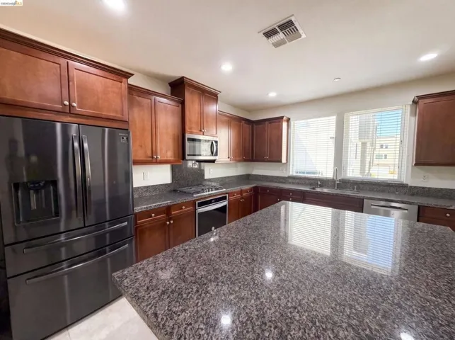 Kitchen featuring a large island, wood cabinetry, stone countertops, and stainless steel appliances including a refrigerator, microwave, gas range, and dishwasher
