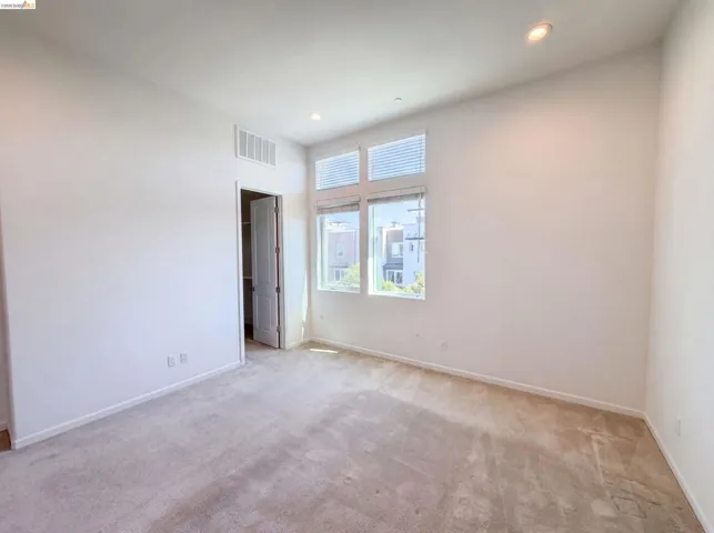 Carpeted room with high ceilings, recessed lighting, and a large window featuring two upper transom windows and a lower window with blinds