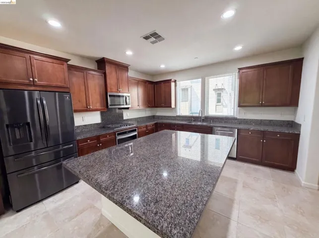 Kitchen featuring an oversized island with a stone-finish countertop, dark wood cabinetry, stainless steel appliances, recessed lighting, and tile flooring