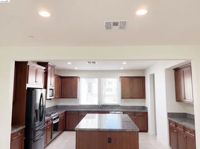 Kitchen featuring rich wood cabinetry, stone countertops, a central island, recessed lighting, and a full suite of dark-finish appliances