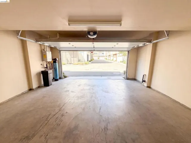 Spacious garage with concrete flooring, automatic garage door opener, overhead fluorescent lighting, and a visible water heater system