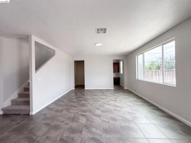 Spacious open concept room featuring large format tile flooring, a wide window with a private backyard outlook, and a staircase with carpeted treads