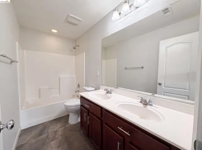 Bathroom featuring a dual-sink vanity with white countertops and dark wood cabinetry, a large wall-mounted mirror, and a combination shower and tub
