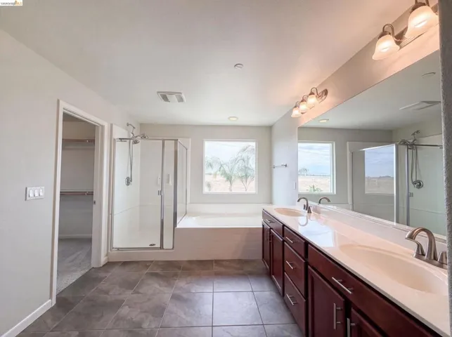 Expansive bathroom featuring a dual vanity with a white countertop and wood-finish cabinetry, a large soaking tub, and a separate glass-enclosed shower
