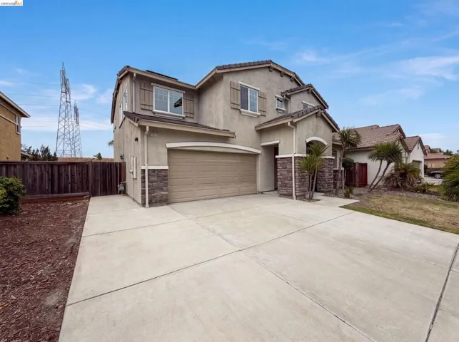 Two-story stucco residence featuring a two-car garage, stone accents, and a concrete driveway