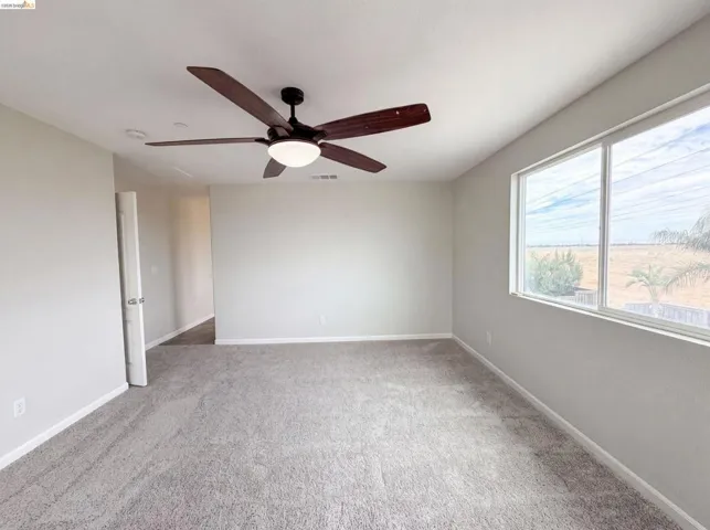 Spacious room featuring neutral carpeting, light-toned walls, and a ceiling fan with integrated lighting