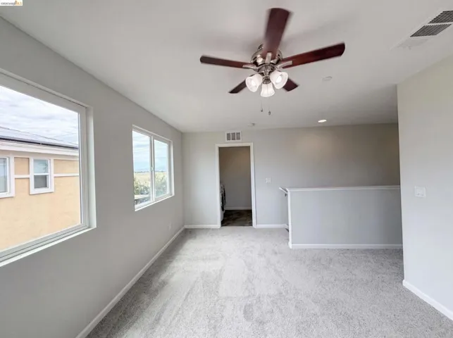 Carpeted room featuring multiple windows, a ceiling fan with light fixture, recessed lighting, and a white railing