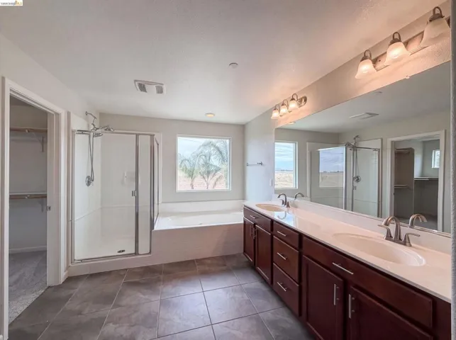 Spacious bathroom featuring a dual vanity with dark wood cabinetry, a large walk-in shower with glass enclosure, a built-in soaking tub, and tiled flooring