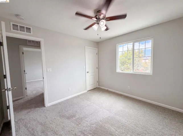 Neutral-toned room featuring a ceiling fan with integrated lighting, a large window with white framing, and light-colored carpet flooring